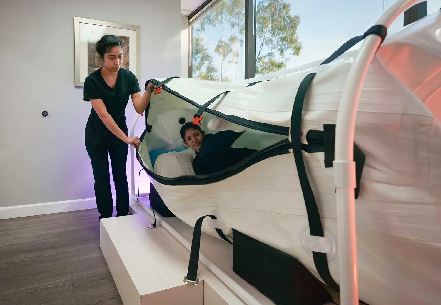 A K Wellness staff member helping someone settle into the sit-down hyperbaric chamber
