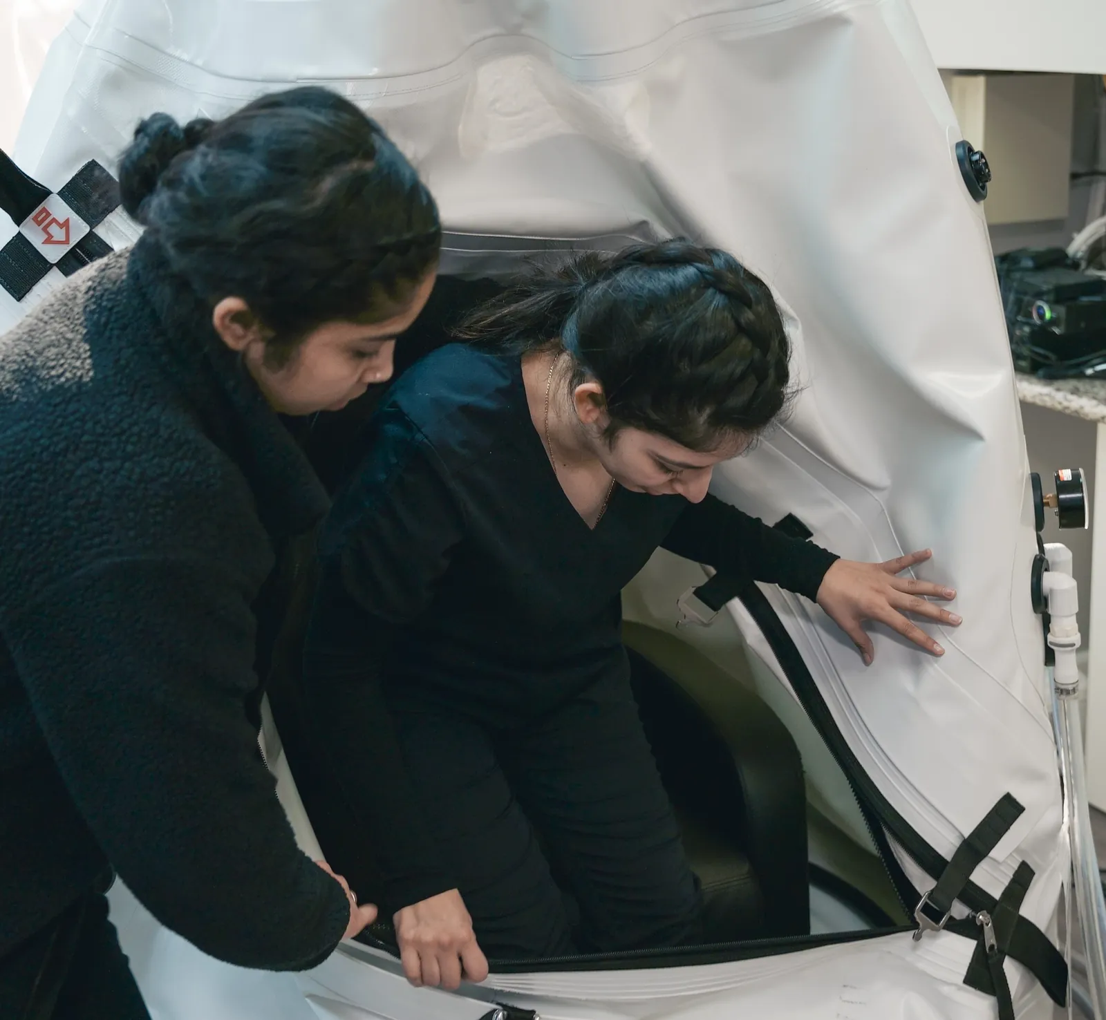 A K Wellness staff member helping someone into the sit-up hyperbaric chamber